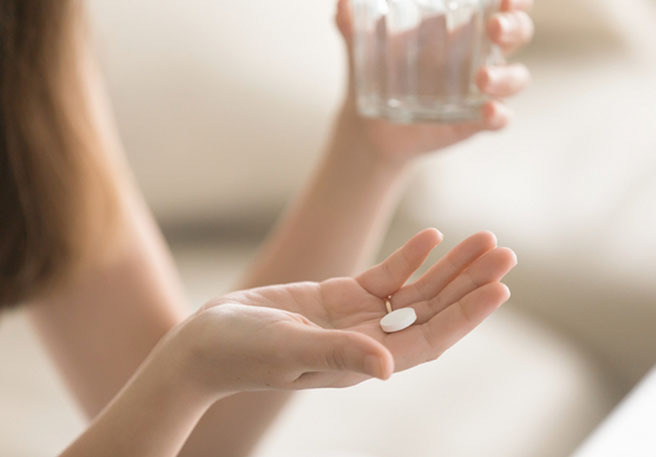 Frau mit Pille und Wasserglas in den Händen