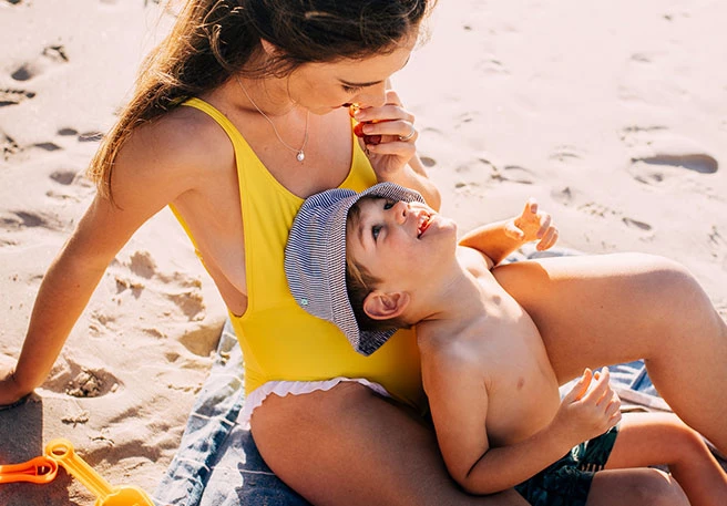 Mutter sitzt mit Kind am Strand Sonnenspray für Kinder Mutter sitzt mit Kind am Strand