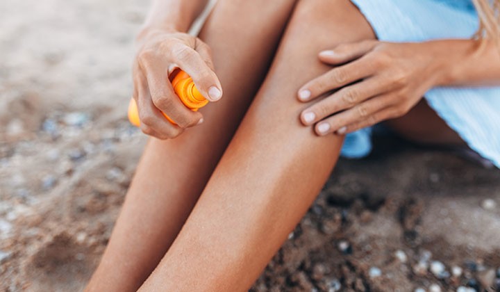Frau mit Sonnenspray Frau am Strand sprüht Sonnenspray auf ihre Beine