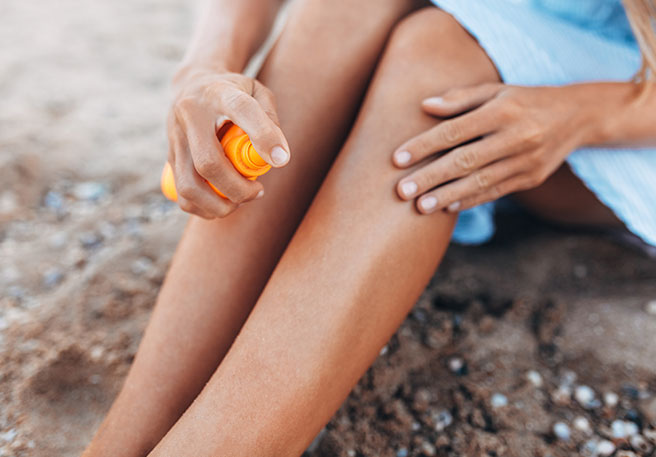 Frau sprüht Beine mit Sonnenschutz ein
