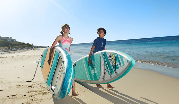 Personen mit SUPs Zwei Personen gehen mit SUPs unter dem Arm am Strand entlang